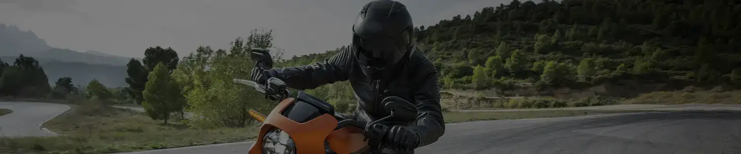 Motorcyclist in black gear rounds a curve on an orange motorcycle on a scenic mountain road, wearing a helmet compatible with the reso pilot pro bluetooth motorcycle helmet headset.
