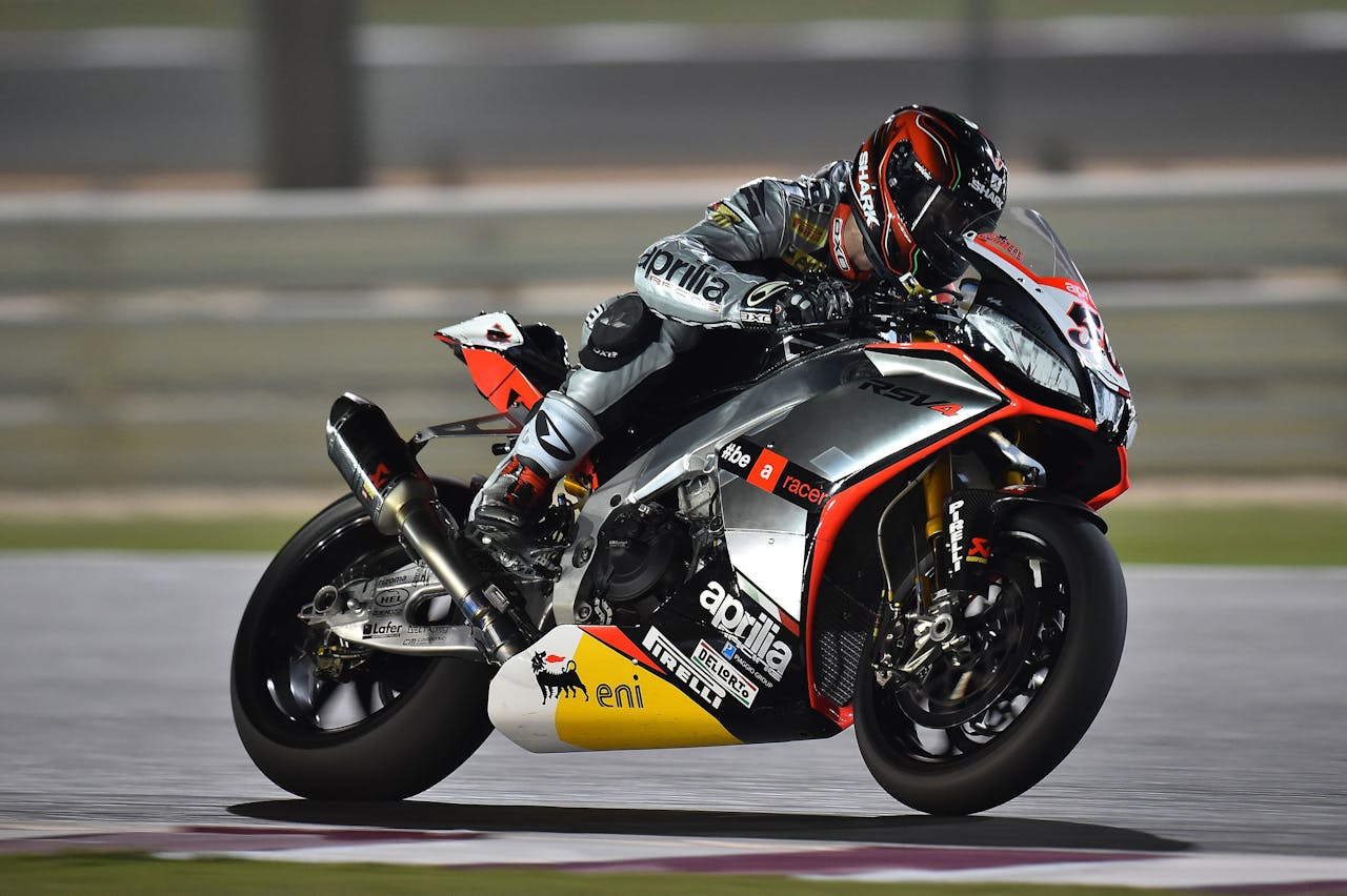 A motorcycle racer wearing a full helmet leans sharply into a turn on a racetrack at night.