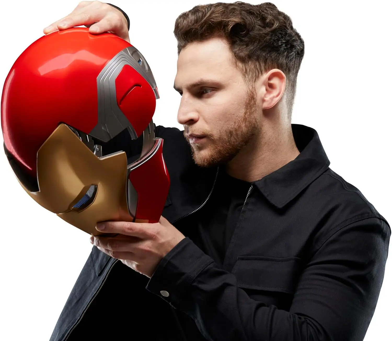 A man with a beard, wearing a black jacket, holds and examines a red and gold Iron Man-themed motorcycle helmet with bluetooth.